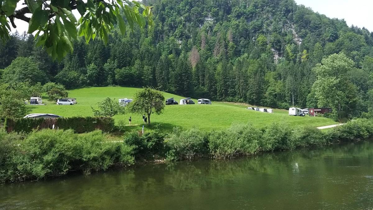 Motorhomes and campervans parked on a grassy riverside flat near Goumois
