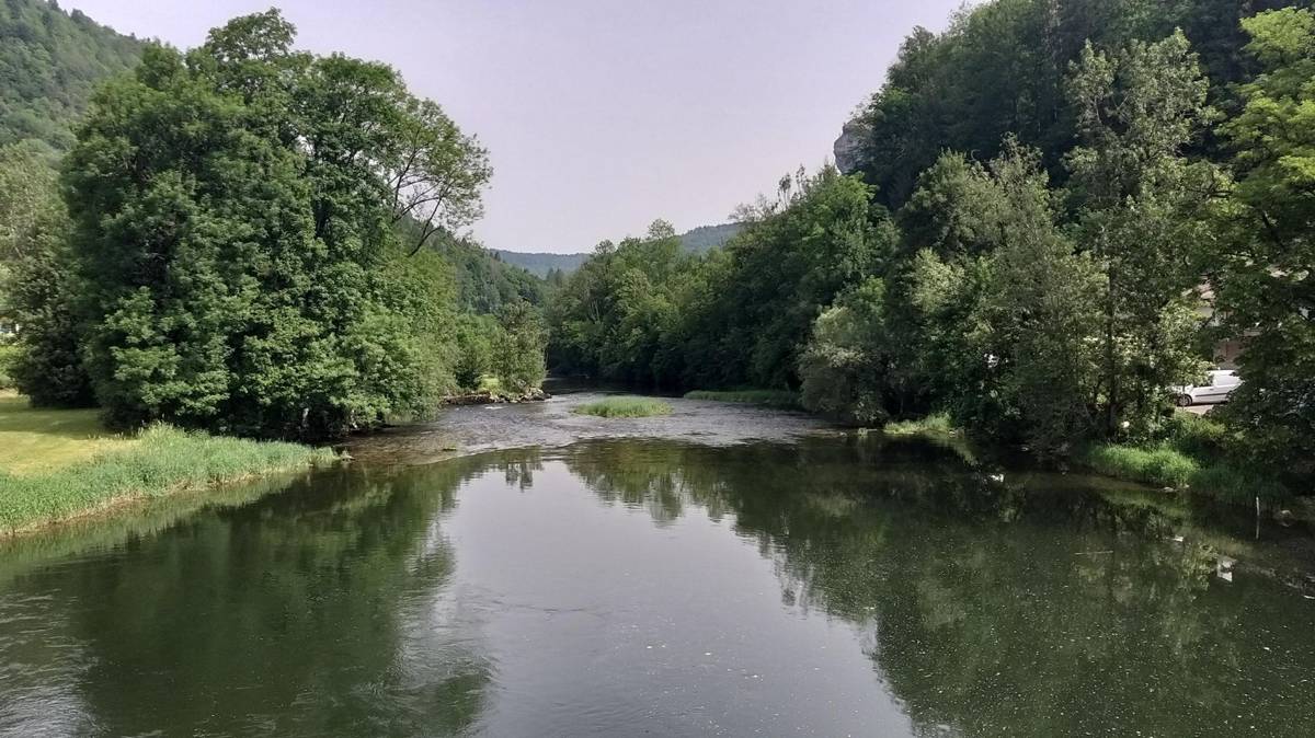 A calm bend in the Doubs river reflecting the wooded valley sides