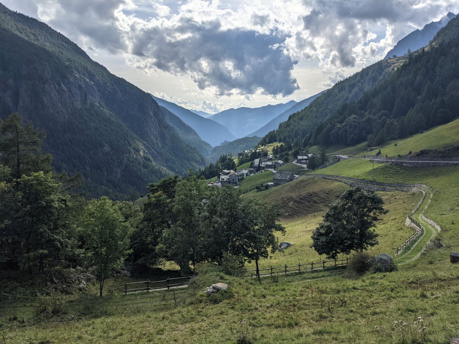 Looking back down the Valpelline valley near Bionaz, a small village on the hillside and forested mountains under a cloudy sky