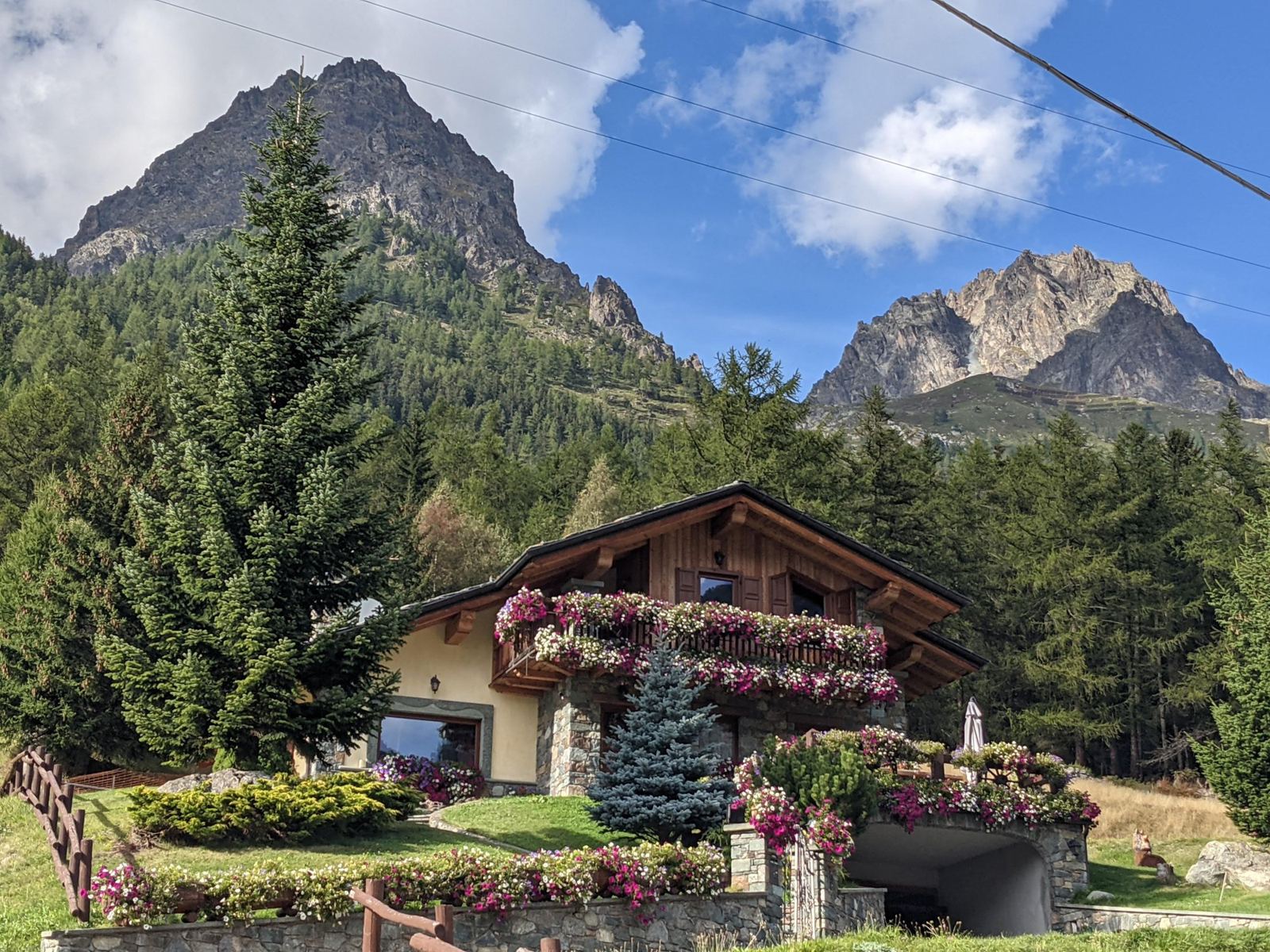 A wooden chalet covered in flower boxes below rocky peaks, between Bionaz and Oyace