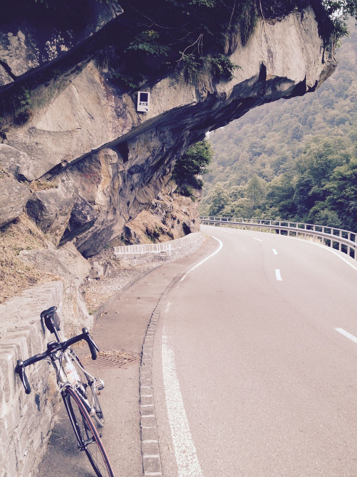 A road bike leaning against a rock overhang beside a mountain road in the Verzasca Valley