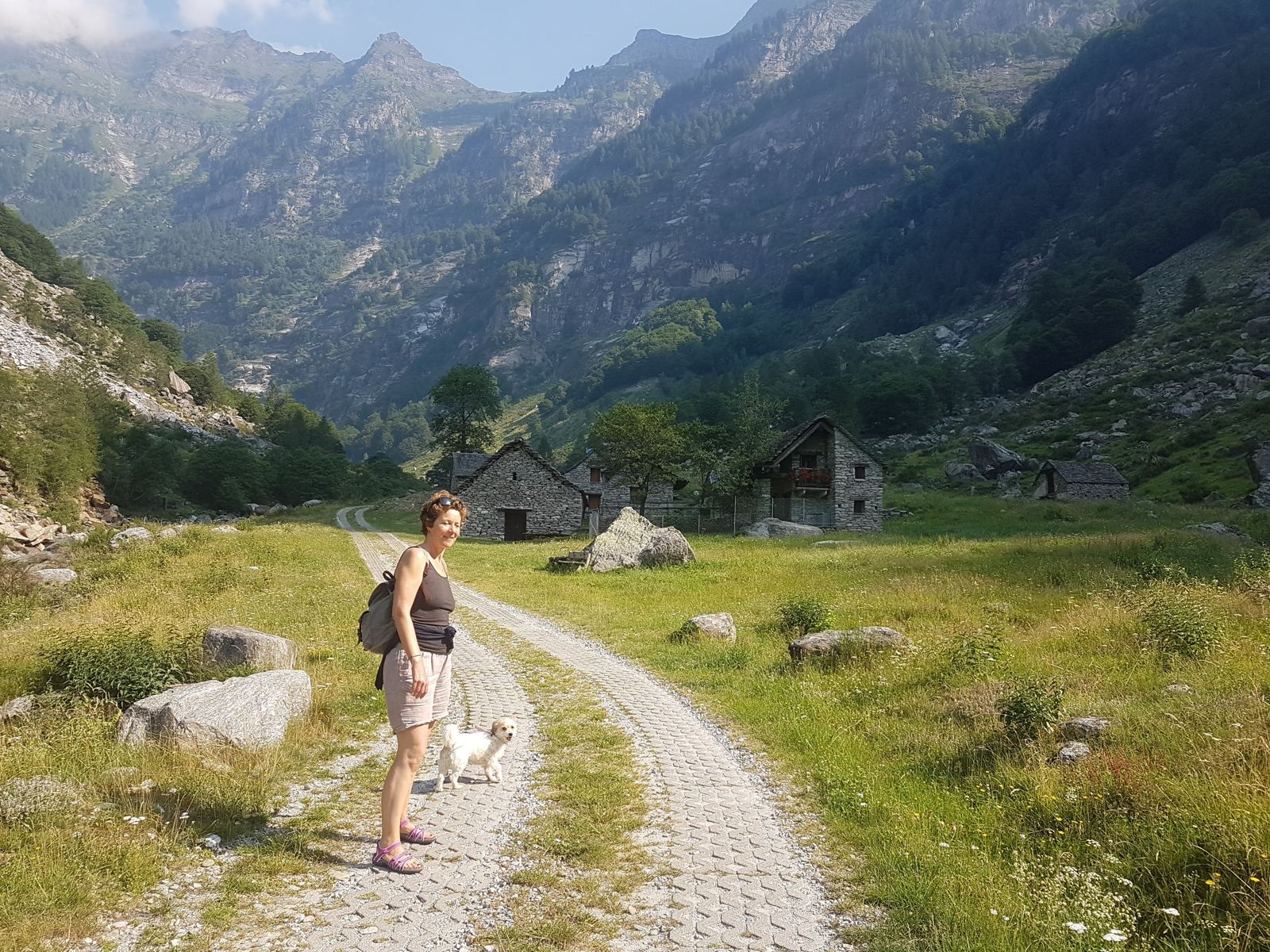 My wife and our dog Lillie walking a gravel track toward a stone hamlet in the Verzasca Valley